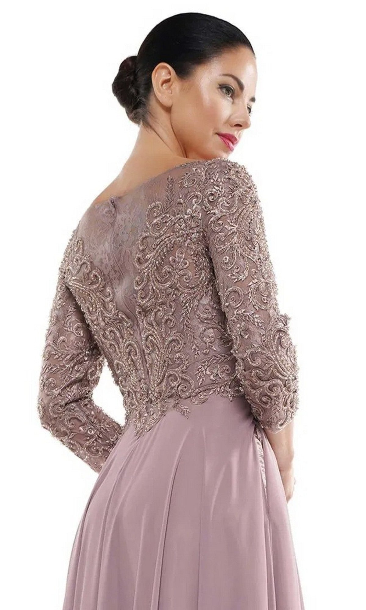 A woman wears the Marsoni MV1052 long formal dress in mauve, featuring a beaded bodice and lace-detailed sleeves, looking over her shoulder against a white background.